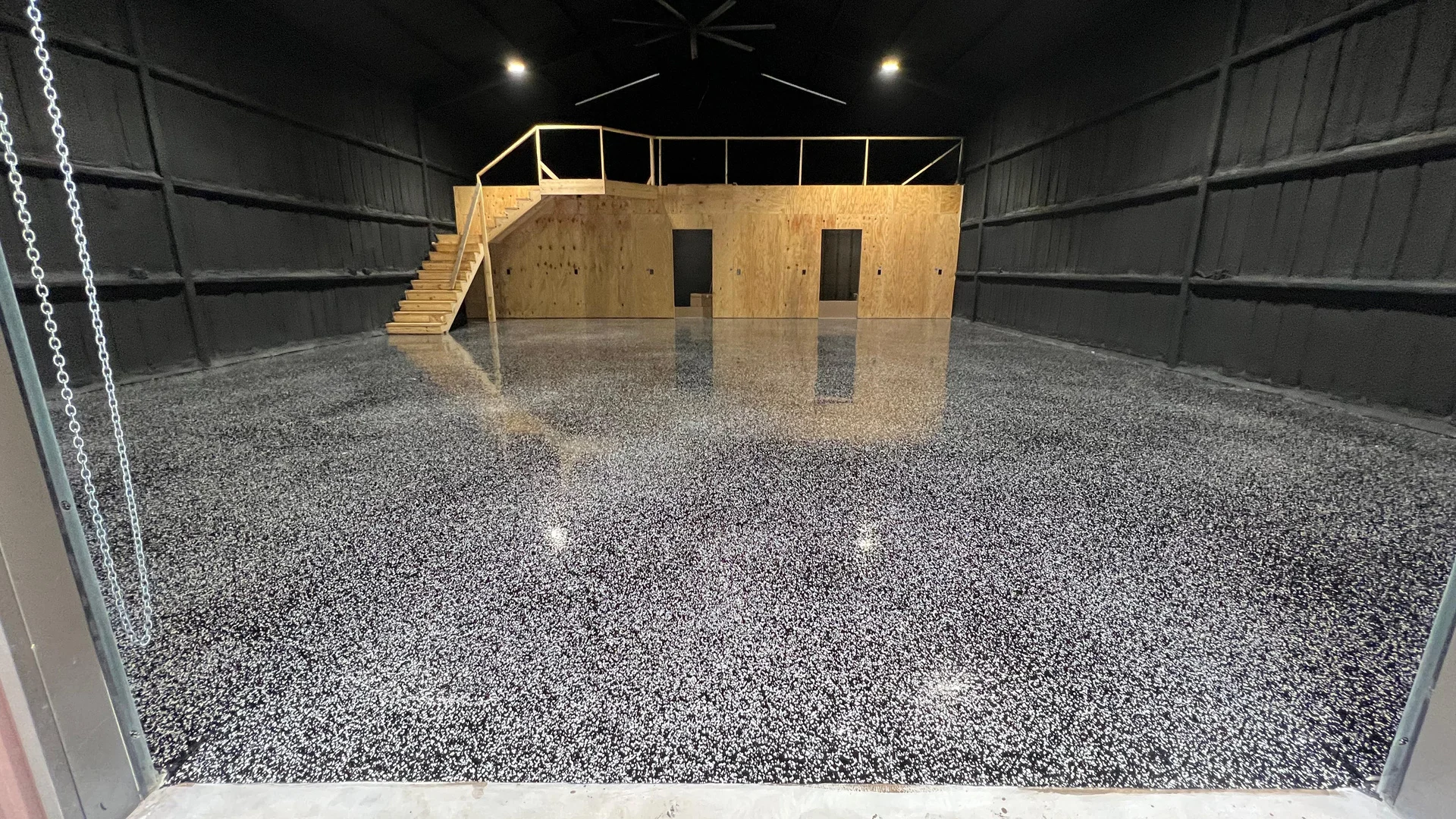 Black flake epoxy floor running the length of a Houston shop beneath a wood mezzanine